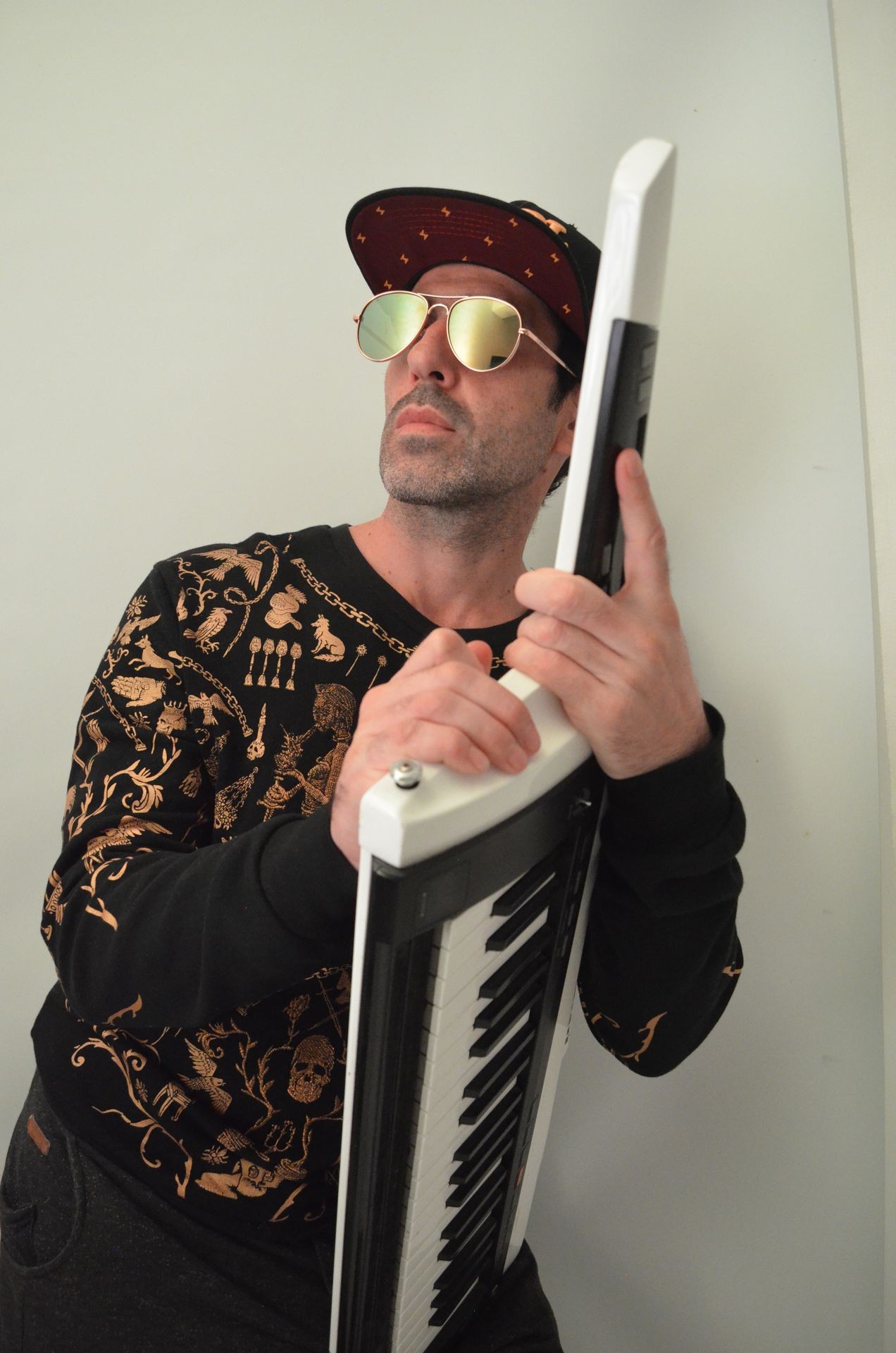 Person holding a keytar wearing sunglasses and a patterned shirt.